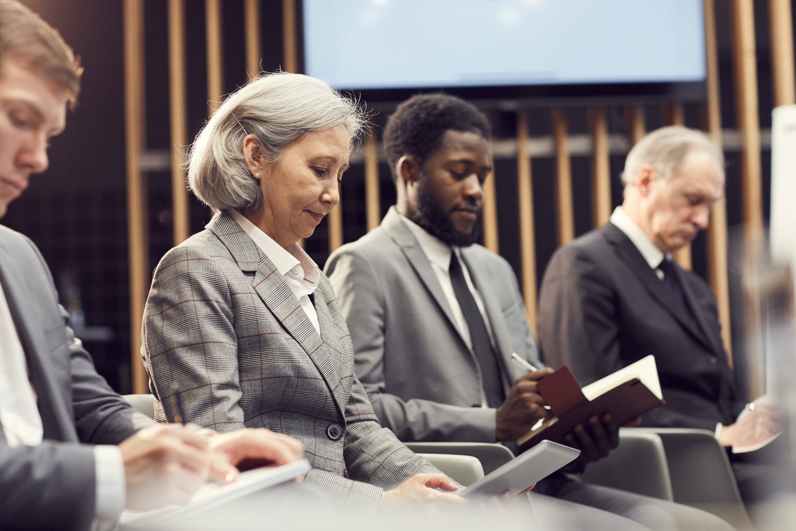 Group of serious multi-ethnic business people sitting in row and making notes while summarizing information at conference